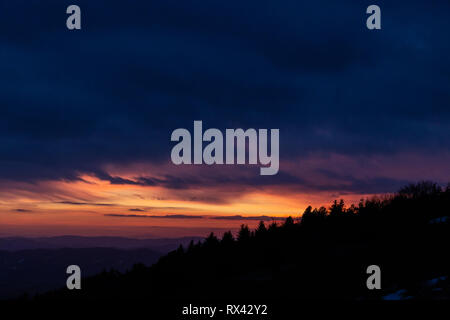 Alberi sagome contro un colore bellissimo cielo al tramonto, con montagne di strati in background Foto Stock