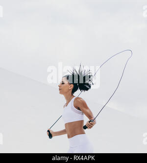 Tagliate il colpo di un atleta femminile in usura fitness lavorando fuori con una corda da salto. Vista laterale di una donna fitness facendo fitness training. Foto Stock