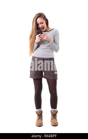 Overjoyed giovane donna elegante urlando durante la lettura e tenendo il telefono cellulare. Corpo pieno isolati su sfondo bianco. Foto Stock