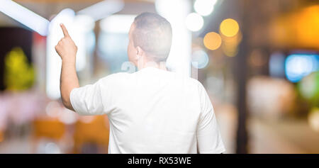 La mezza età uomo arabo wearig t-shirt bianco su sfondo isolato in posa rivolta indietro dietro con il dito mano Foto Stock