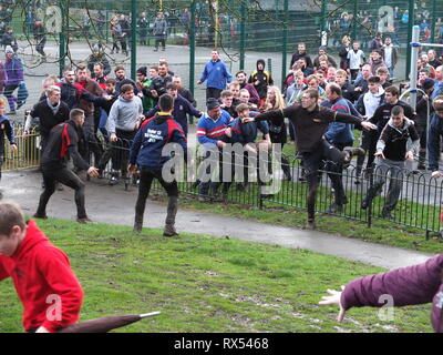 Ashbourne Shrovetide Football 2019. I giocatori scramble a seguire la palla il gioco entra in un parco giochi per bambini durante il Mercoledì delle Ceneri gioco. Foto Stock