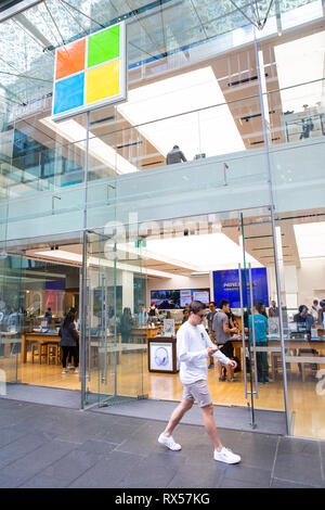 Uomo che guarda un telefono cellulare passeggiate passato Microsoft tecnologia flagship store in Pitt Street, Sydney, Australia Foto Stock