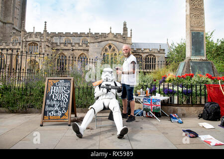 Un residente vestito come un Stormtrooper di Star Wars con il barbiere di strada offrendo gratuitamente per tagli per i senzatetto nella High Street, Glastonbury Regno Unito Foto Stock