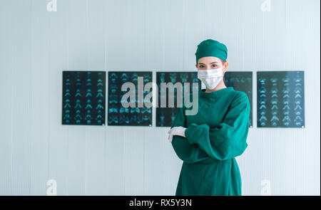 Ritratto di donna medico chirurgo in verde frega mettendo su guanti chirurgici e guardando la fotocamera . Giovani asiatici medico donna con immagine a raggi x backgro Foto Stock