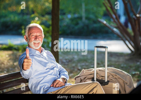 Senior gentleman seduto su una panca in legno e rilassante in un parco Foto Stock