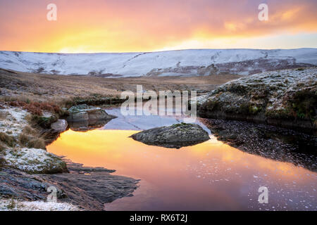 Pont Ar Elan, Elan Valley, il Galles. Snowy scena di Afon elan fluente verso craig goch sotto orange sunrise con la riflessione del cielo Foto Stock