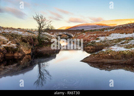 Pont Ar Elan, Elan Valey, Galles snowy scena di Afon Elan che fluisce attraverso un ponte in inverno con Lone Tree riflessa nell'acqua e la mattina presto li sun Foto Stock