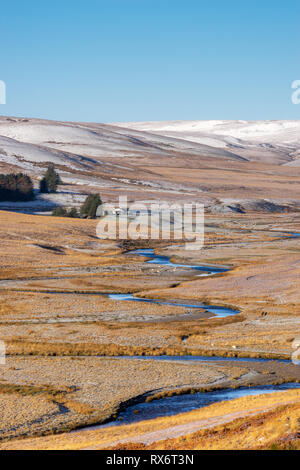 Pont Ar Elan, Elan Valley, il Galles. Snowy scena di Afon elan fiume avvolgimento attraverso il paesaggio di montagna con la fattoria edificio a distanza Foto Stock