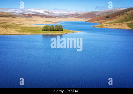 Craig Goch serbatoio in Elan Valley Galles con neve montagna sormontata e alberi. Acqua di approvvigionamento di Birmingham che riflette il cielo blu Foto Stock