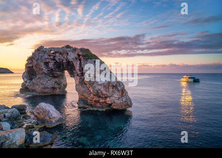 Es Pontas in Mallorca con barca ancorata nelle vicinanze del mare Mediterraneo. Sunrise con sun glinting off lo yacht e rock arch. Foto Stock