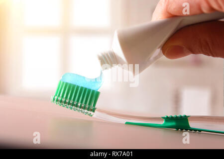 Concetto di igiene orale con mano mettendo il dentifricio su uno spazzolino da denti sulla tavola di legno in bagno. Composizione orizzontale. Vista frontale. Foto Stock