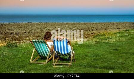 Coppia in vacanza al mare rilassandosi su sdraio colorate in una serata estiva a Devon.England.UK Foto Stock