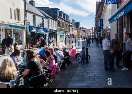 Gruppo di persone sedute al di fuori di bracci di volontariato bar in Fort William high street lochaber godendo il sole Scotland Regno Unito Foto Stock