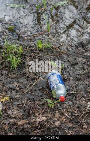 Plastica scartati bibite analcoliche bottiglia in un angolo di un campo umido nella campagna del Regno Unito. Foto Stock