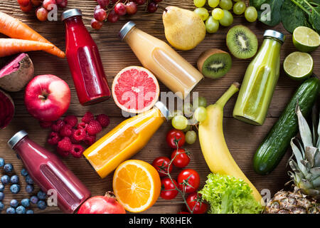 Frullati colorati in bottiglie e frutta fresca e verdure su woodentable, vista dall'alto. Foto Stock