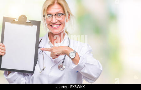 La mezza età bionda medico donna azienda appunti su sfondo isolato molto felice puntando con mani e dita Foto Stock