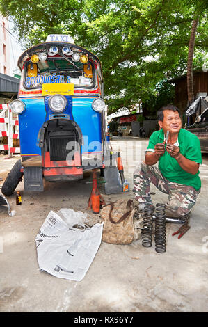 Bangkok, Thailandia: Close-up di una coloratissima-Tuk Tuk veicolo, isolato da altro traffico, sotto la riparazione su per la strada con il suo driver Foto Stock