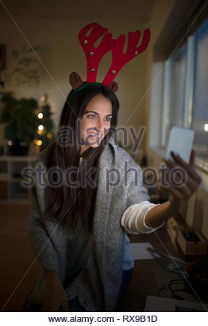 Felice giovane donna nel natale renne palchi tenendo selfie con la fotocamera del telefono in camera oscura