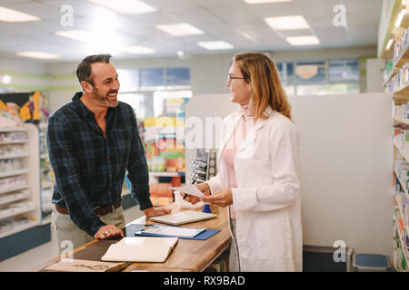 Il cliente a parlare con la femmina chimico presso il Drug store. Il farmacista aiutando i clienti di sesso maschile in farmacia. Foto Stock