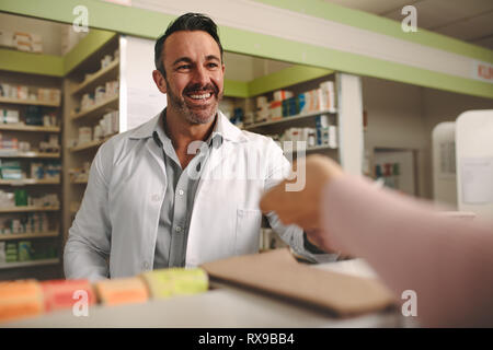 Il cliente consegna una prescrizione medica per la sorridente farmacia maschio in piedi dietro il contatore. Farmacia tenendo la prescrizione da parte del cliente in farmacia. Foto Stock