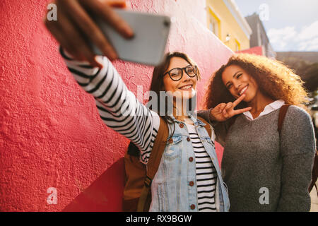 Fidanzate rendendo selfie all'esterno. I viaggiatori femmina tenendo selfie con un telefono cellulare. Foto Stock