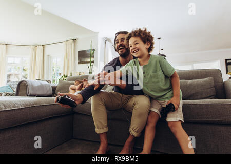 Padre e figlio divertendosi video gioco a casa. L'uomo la riproduzione del video gioco con Figlio seduto sul divano di casa azienda joystick. Foto Stock