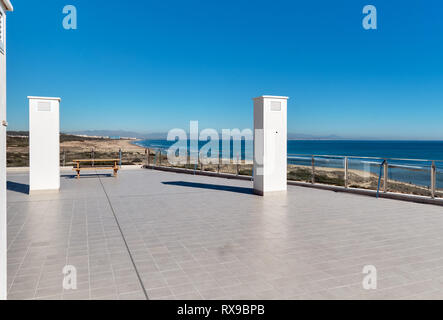 Vuoto spaziosa terrazza piastrellata pavimento grigio trasparente come il vetro recinzione di confine e lonely banco con bella vista al mare mediterraneo blu chiaro Foto Stock