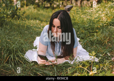 Angolo di alta vista di donna con capelli lunghi utilizzando il telefono cellulare mentre giaceva sul campo erboso in giardino Foto Stock