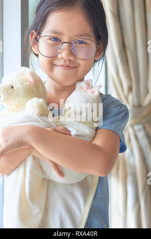 Ritratto di ragazza sorridente indossando occhiali abbracciando orsacchiotti a casa Foto Stock