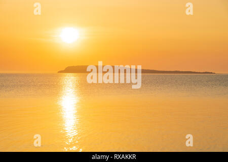 Il sorgere del sole attraverso la foschia sopra Bear's scamone isola in Georgian Bay trasforma il cielo e acqua di un bel colore dorato, Fathom cinque National Marine Park, Ontario, Canada Foto Stock