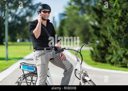 Imprenditore sulla bicicletta elettrica parlando al telefono Foto Stock