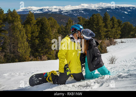 Paio di baciare in ginocchio sulla coperta di neve montagna contro gli alberi nelle foreste Foto Stock