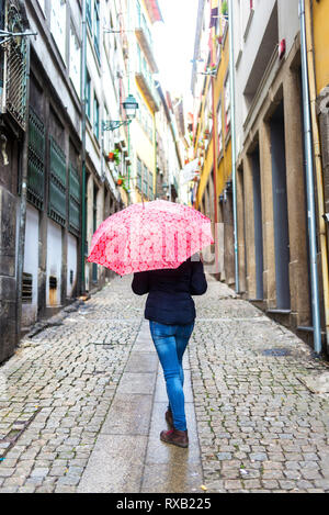 Vista posteriore della donna con ombrello camminando sul sentiero in mezzo a edifici in città Foto Stock