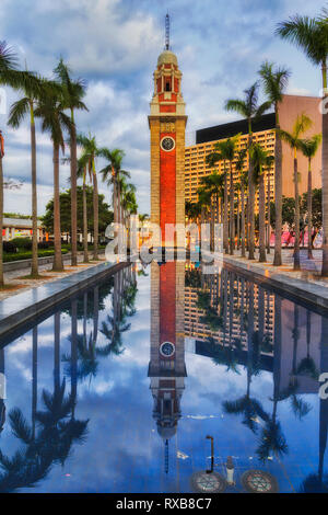 Patrimonio storico orologio delle Ferrovie nella torre della città di Hong Kong Tsim Sha Tsui di Kowloon con piscina di acqua e palme che riflette contro il cielo blu. Foto Stock