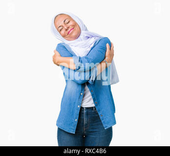 La mezza età araba orientale donna che indossa arabian hijab su sfondo isolato abbracciando sé felice e positivo, sorridente fiducioso. Auto amore e auto Foto Stock