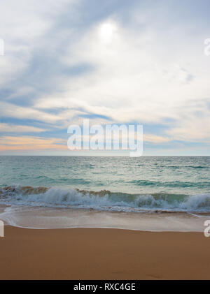 Seascape pacifica con le onde che lambiscono dolcemente a riva sulla sabbia. Sole acquoso filtra attraverso la nube luminosa che copre il cielo Foto Stock