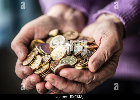 Titolare di pensione o di rendita donna tenendo in mano delle monete in euro. Il tema delle pensioni basse. Foto Stock