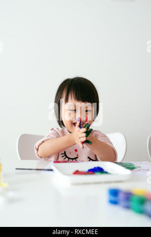 Poco ragazza asiatica pittura con pennello e vernici colorate Foto Stock