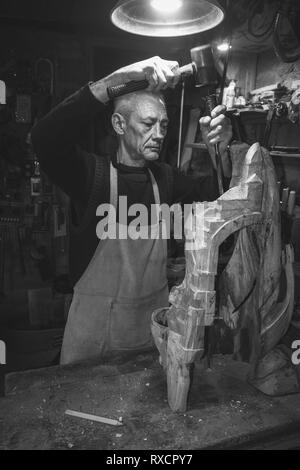 Maestro di legname 50 - 55 anni crea la scultura in legno in officina, la fotografia in bianco e nero Foto Stock