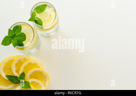 Vista da sopra il decor delle due bevande fredde, piatto pieno di fette di limone con foglie di menta e copia spazio su uno sfondo bianco. Foto Stock