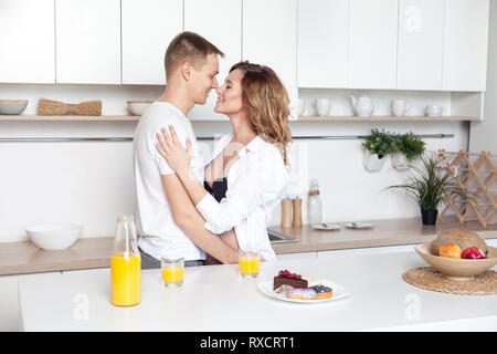 I giovani coniugi abbraccia in piedi vicino a tavola in cucina. Il marito abbraccia la sua moglie incinta, mettendo le mani sul suo grande pancia, ai genitori di godere ogni o Foto Stock