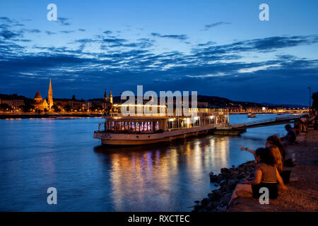 Ungheria, città di Budapest, persone di ritrovo al fiume Danubio waterfront sulla tranquilla serata, crociera e cena in barca, vista da Pest a Buda. Foto Stock