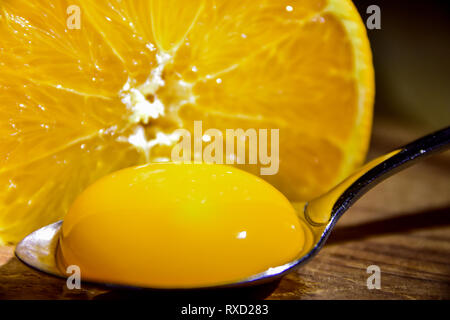 Close-up di un giogo di uova in un cucchiaio d'argento nella parte anteriore di un'arancia a fette in una metà Foto Stock