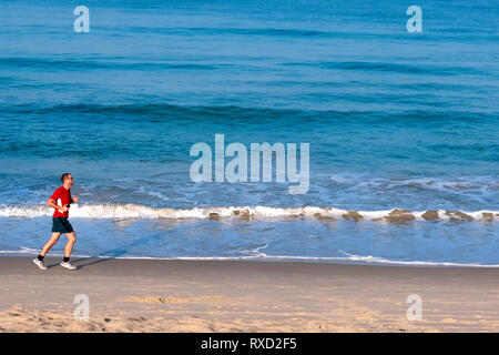 In un inizio di mattina a Bang Tao Beach, Phuket, Thailandia, un pareggiatore corre lungo il litorale Foto Stock