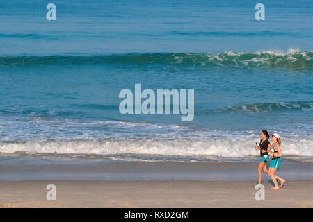 In un inizio di mattina a Bang Tao Beach, Phuket, Thailandia, due femmine pareggiatore di correre lungo il litorale Foto Stock