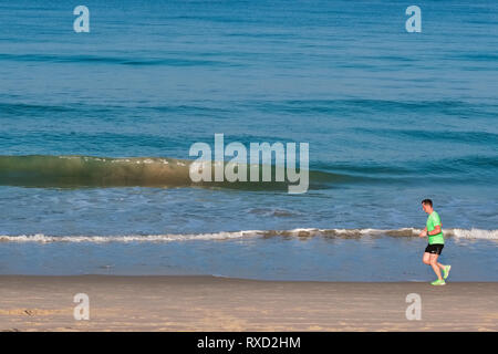 In un inizio di mattina a Bang Tao Beach, Phuket, Thailandia, un pareggiatore corre lungo il litorale Foto Stock