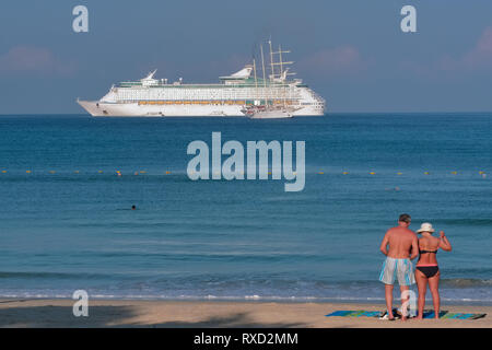 Su una prima mattina, un turista occidentale giovane sorge sulla spiaggia di Patong, Phuket, Thailandia, come una grande nave da crociera è ancorata al largo Foto Stock