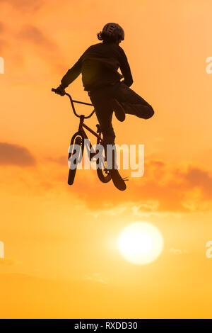 Biker con casco esegue trucco mid-aria. Sunset bmx fun Foto Stock