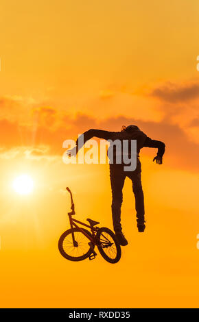 Silhouette di uomo facendo cadere la sua moto mentre in una metà di salto in aria. Stunt andato storto Foto Stock