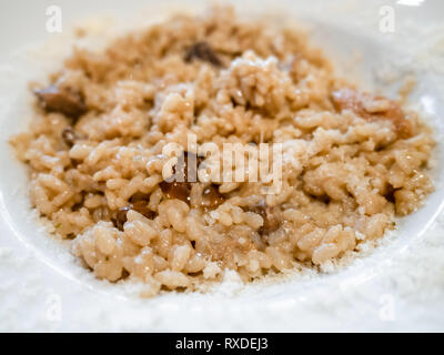 Cucina Italiana - risotto con funghi porcini (riso bollito con funghi porcini) nella vaschetta bianca in un ristorante locale in Lombardia Foto Stock